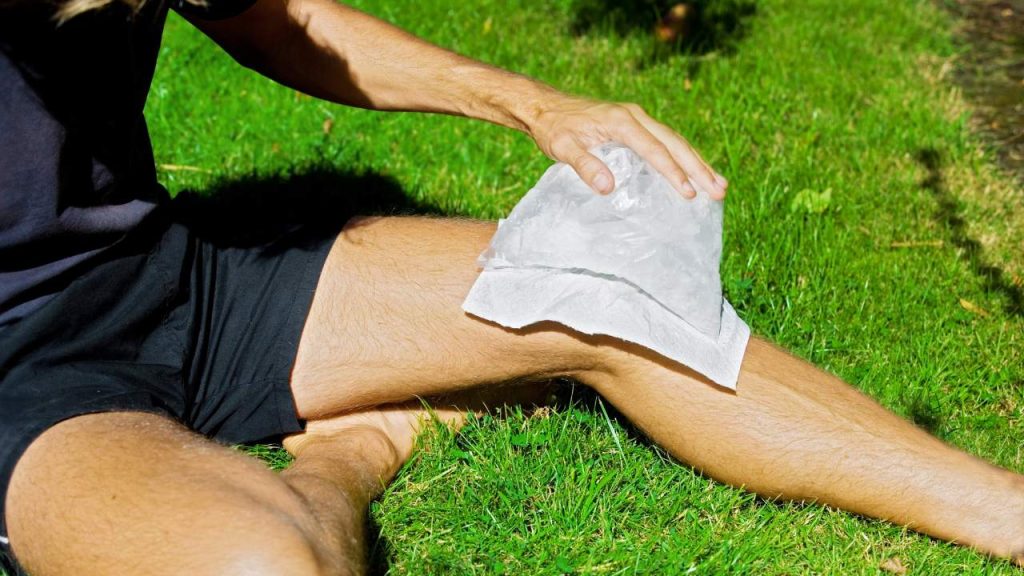 A male athlete icing his knee illustrating a common running injury and short term treatment for runner's knee