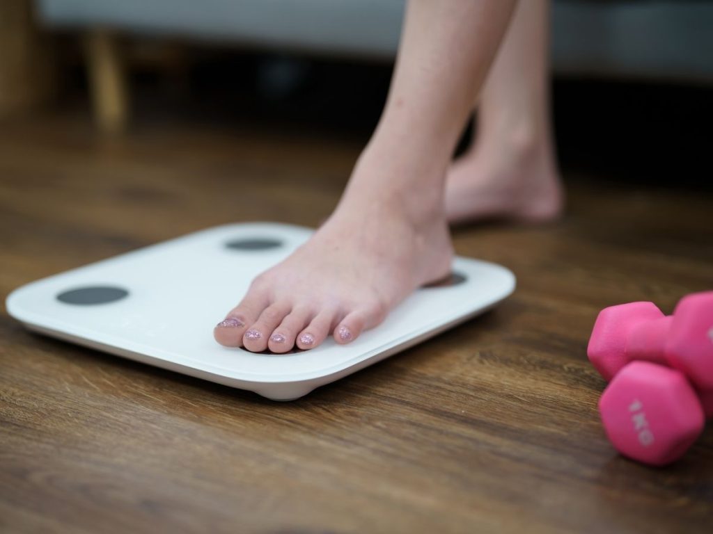 A runner stepping on the scale to check their body fat percentage - a predictor of racing times